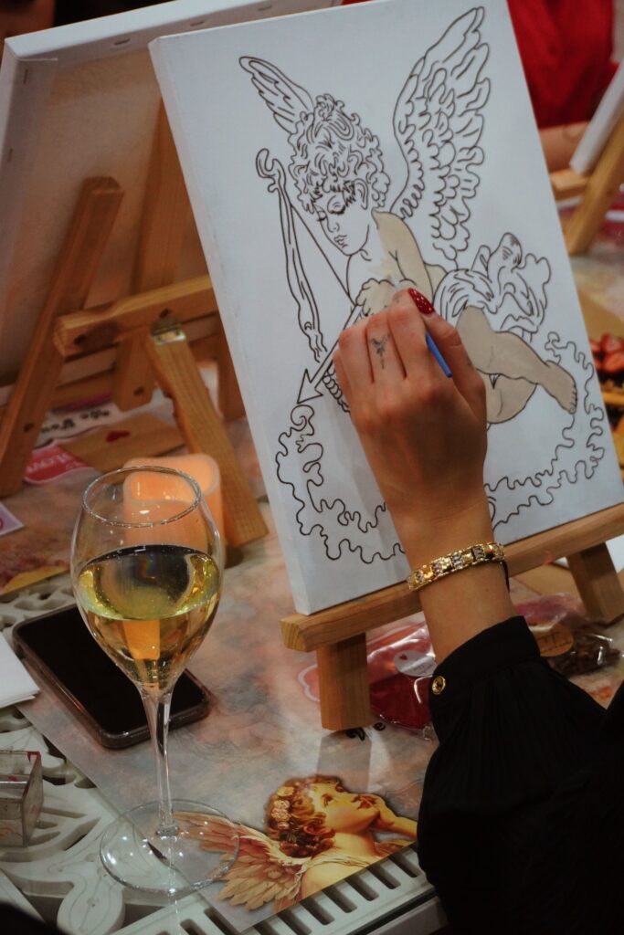pexels-photo-29246210-29246210 Artist painting a Cupid on canvas in art workshop with wine in hand, capturing creative atmosphere.